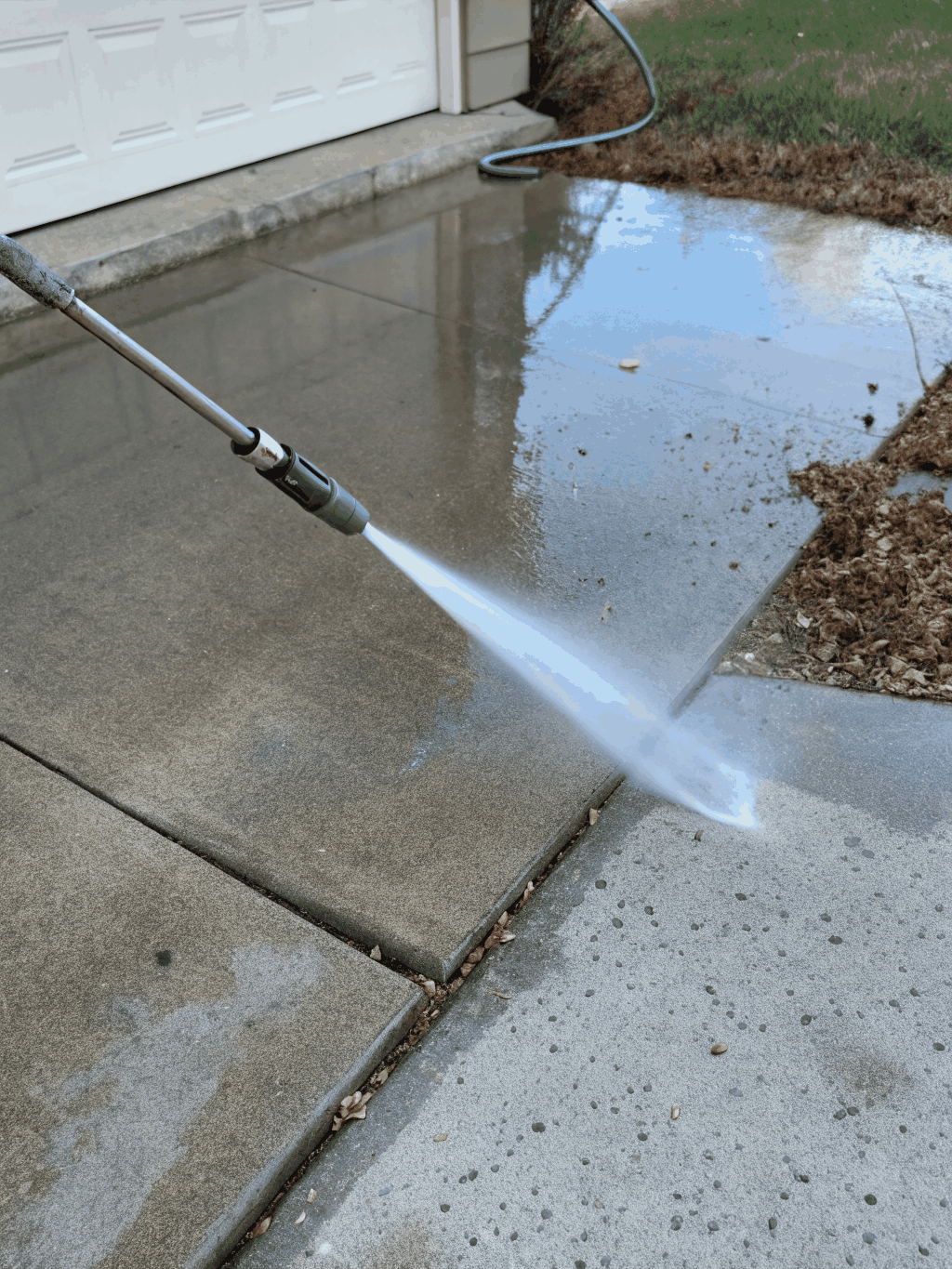 High-pressure water stream cleaning a concrete driveway surface